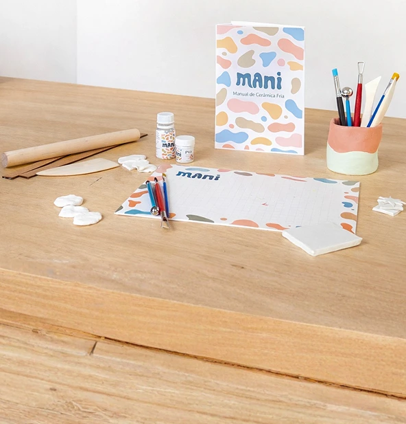 Kit completo de cerâmica fria Mani — manual, ferramentas e materiais sobre mesa de madeira